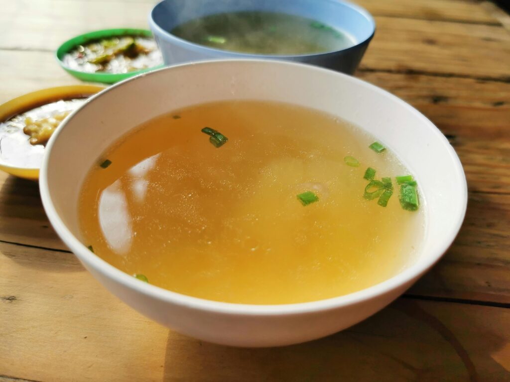 Delicious homemade soup garnished with scallions in a bowl on a rustic wooden table.