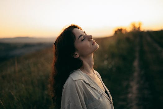 A serene woman with head tilted back, savoring the warm sunset in a field.