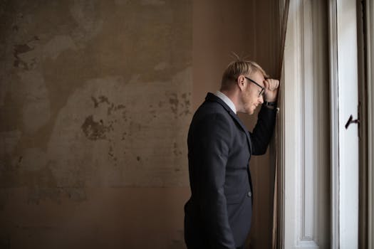 A worried businessman in a suit leaning against a window, expressing stress and concern.