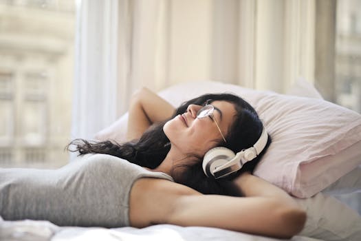 A woman with headphones lying on a bed, enjoying music in a relaxed, cozy setting.