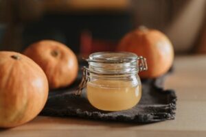 A cozy still life with homemade apple cider in a glass jar surrounded by pumpkins on a wooden table.