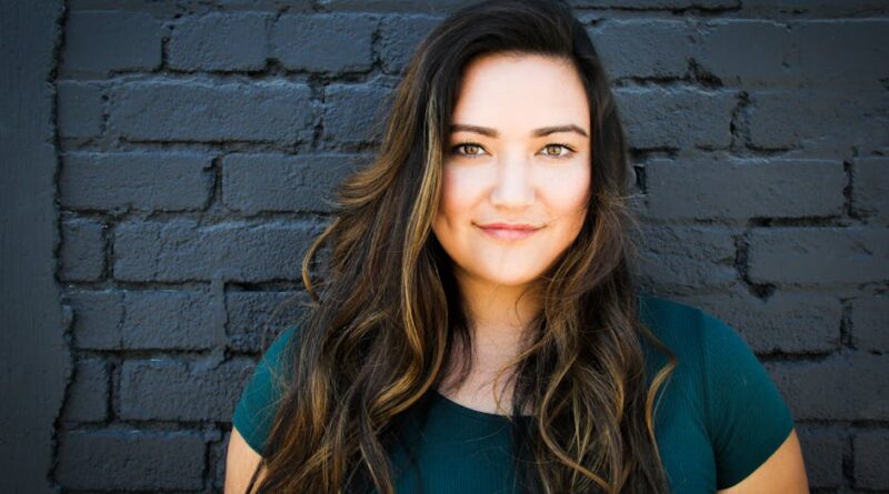 A captivating portrait of a woman smiling confidently in front of a brick wall, showcasing her long brunette hair and vibrant eyes.