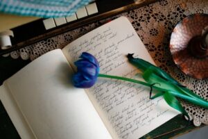 A blue tulip rests on an open journal with handwritten notes, beside a vintage candle.