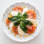 Fresh Caprese salad with tomatoes, mozzarella, and basil on a decorative plate.