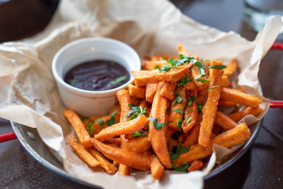 Close-up of crispy sweet potato fries garnished with parsley served with a dip.