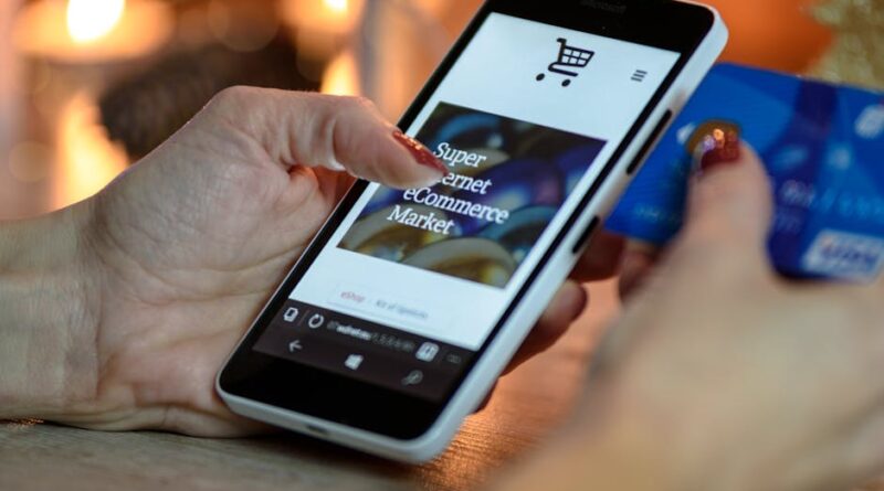 Woman using smartphone for online shopping with credit card in hand, festive background lighting.