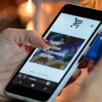 Woman using smartphone for online shopping with credit card in hand, festive background lighting.