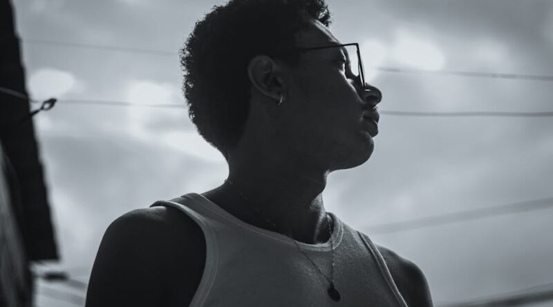 Dramatic side profile silhouette of a reflective young man wearing glasses and a necklace outdoors.