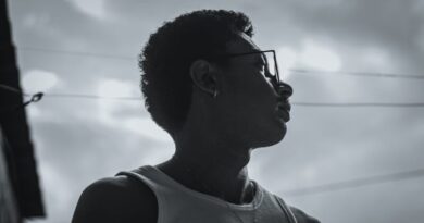 Dramatic side profile silhouette of a reflective young man wearing glasses and a necklace outdoors.