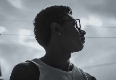 Dramatic side profile silhouette of a reflective young man wearing glasses and a necklace outdoors.