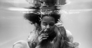 Black and white unemotional young female in loose dress diving with eyes closed into seawater