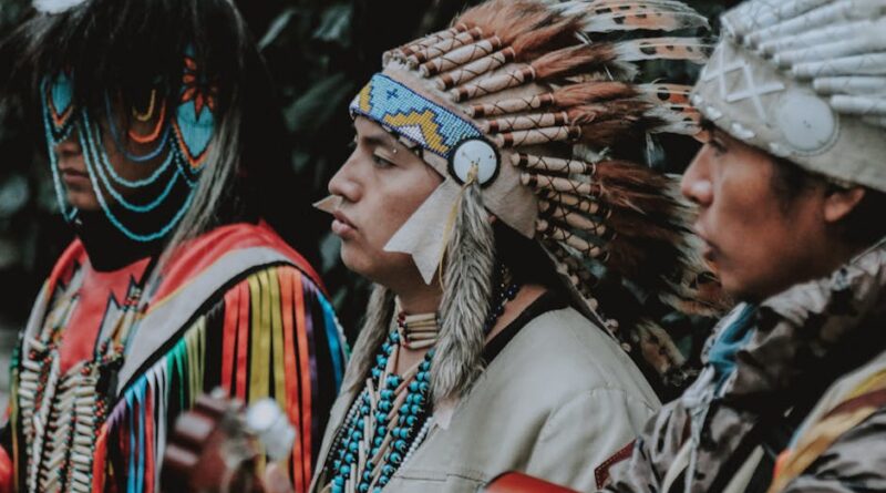 Three Native American men in traditional attire play guitars outdoors, capturing a cultural musical moment.