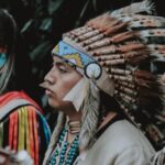 Three Native American men in traditional attire play guitars outdoors, capturing a cultural musical moment.