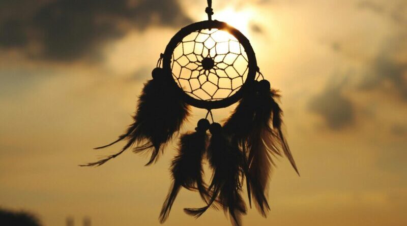 Silhouette of a dreamcatcher hanging against a serene sunset sky.