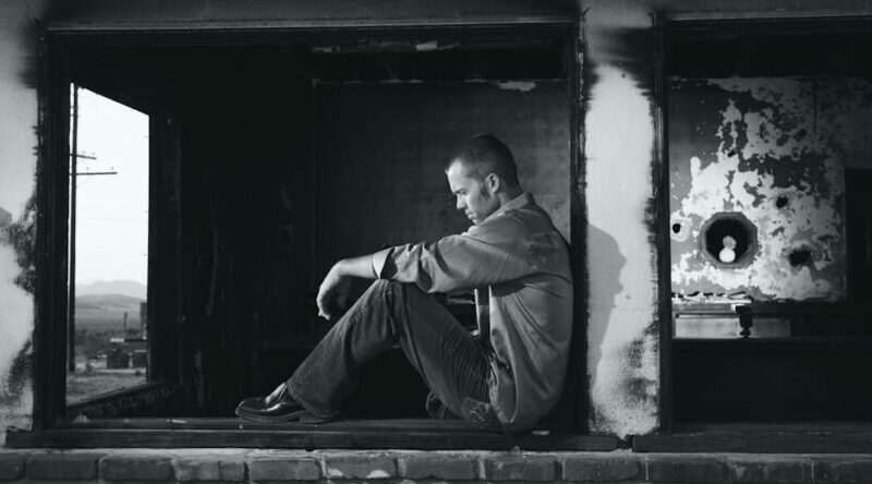A young man sits pensively in a derelict building, embodying solitude and contemplation.